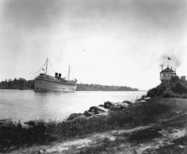 The screw passenger cruise vessel, "South American," in a channel. Shore and lighthouse in foreground.