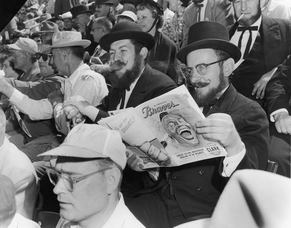 Two men sitting in the stands review the Milwaukee Braves official program during a game.