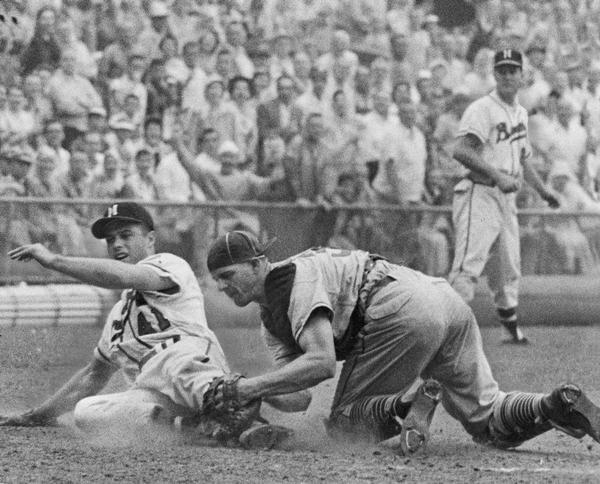 Eddie Mathews, third baseman for the Milwaukee Braves baseball team, sliding into home plate. Chicago Cubs catcher Cal Neeman is applying the tag as Braves third base coach, Connie Ryan is looking on.