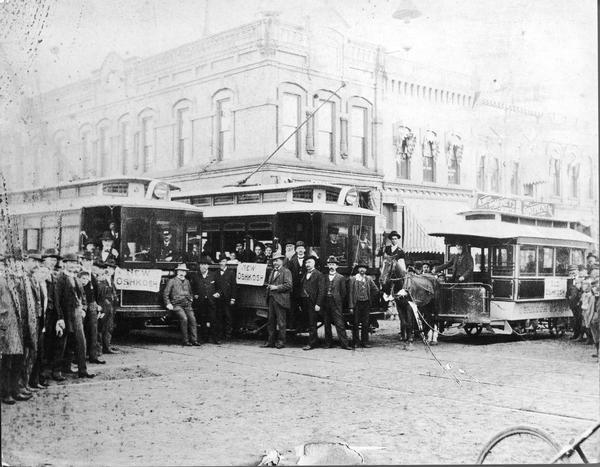 A large group of people posing with "Old Oshkosh," a horse-drawn streetcar, and "New Oshkosh," an electric trolley.