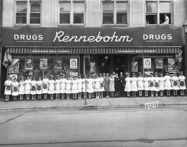 Employees of Rennebohm Drug Store #2, 204 State Street, photographed in front of the store. The majority of the employees are waitresses. War bond posters are in the store windows.