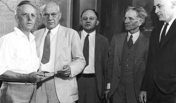 Neils Ruud, 824 E. Dayton Street, receiving the first unemployment compensation check issued in Wisconsin from Voyta Wrabetz, chairman of the state industrial commission. Also shown is Edwin Witte, university economist and author of the national social security act, Professor John Commons, university economist, and Ruud's employer H.H. Brockhausen.