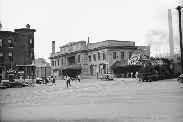 Exterior view of the Chicago & Northwestern railroad station, 219 S. Blair St., along with the Lake View Hotel, 524 E. Wilson St, in Madison. A man holding a stop sign is in the road between the buildings.
