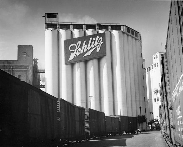 Grain elevator with large Schlitz sign. There are railroad cars on a railroad track in the foreground.