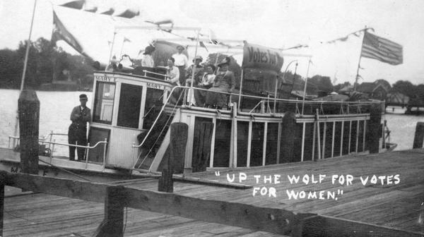 Suffragists sitting aboard the <i>Mary E.</i> at dockside on the Wolf River. The boat sports a banner reading: "Votes for Women."