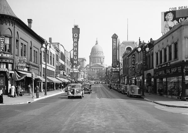 Wisconsin State Capitol from 200 Block of State Street A view from the 200 block of State Street looking toward the Wisconsin State Capitol. This urban scene includes marquees for the Orpheum Theatre and the Capitol Theatre, storefronts, traffic, and pedestrians.
