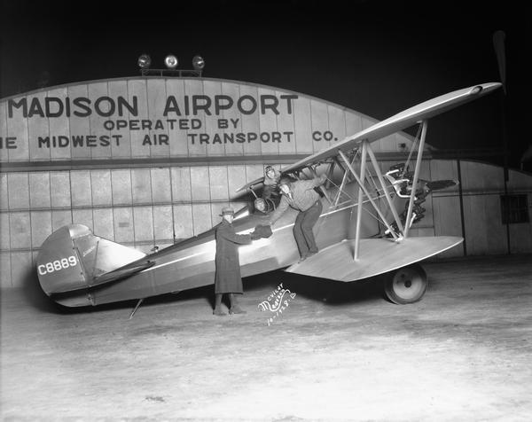 Travelair plane returning to the Madison Airport from a Wisconsin v. Purdue football game. Here photographer Aldro Wasley is handing photographs of the game to a "Capital Times" representative. Pilot Orland G. Corben and another passenger are in the background.