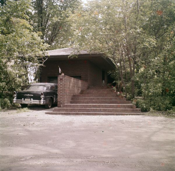 Exterior of the of the Malcolm E. Willey residence showing the entrance steps and a portion of the carport.  A black car is parked in front of the carport.  The residence was designed by Frank Lloyd Wright.