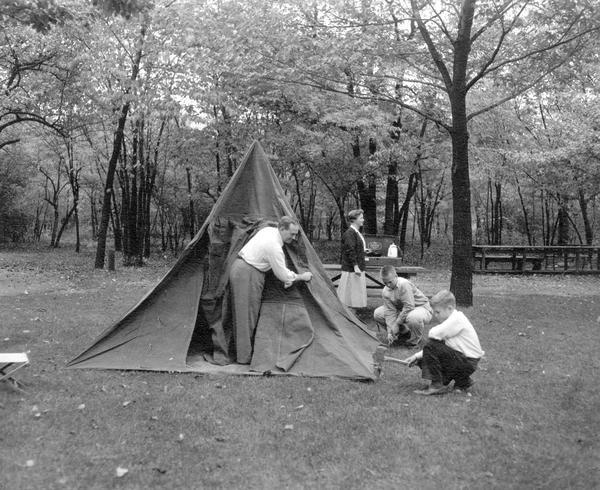 Man, woman and two children putting up a tent by some trees.