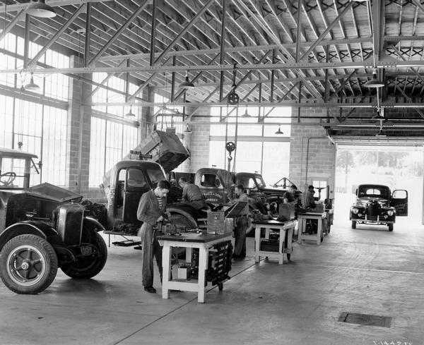 Mechanics working inside the service center of an International Harvester dealership. The door of one of the trucks is painted "McCormick-Deering Store."