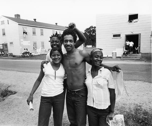 Four smiling young Cubans with petitions for camp nomination elections. Photographs made on July 4, 1980, by Archibald of Cuban refugees who had arrived as a result of the Port of Mariel exodus, and were housed at Camp McCoy, Wis.; including images of the camp life of Cuban men, women, and children.