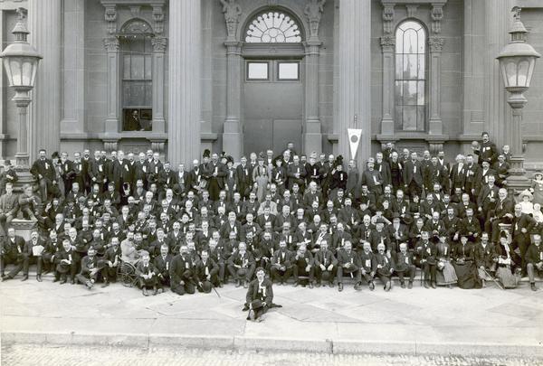 A group portrait of Civil War veterans and their families pose in front of the Milwaukee armory building at the reunion of The Iron Brigade.