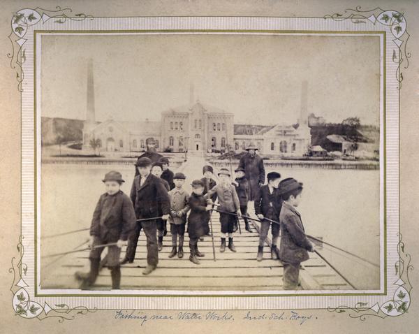 Group of young boys and two adult men fishing near the Water Works of the State Industrial School for Boys.