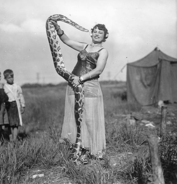 A female snake charmer with the Cole Brothers Circus, watched by two children.