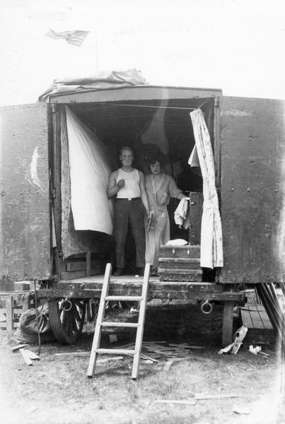 A man and a woman, in the process of getting dressed for a circus performance, pose informally in the back of a circus wagon.