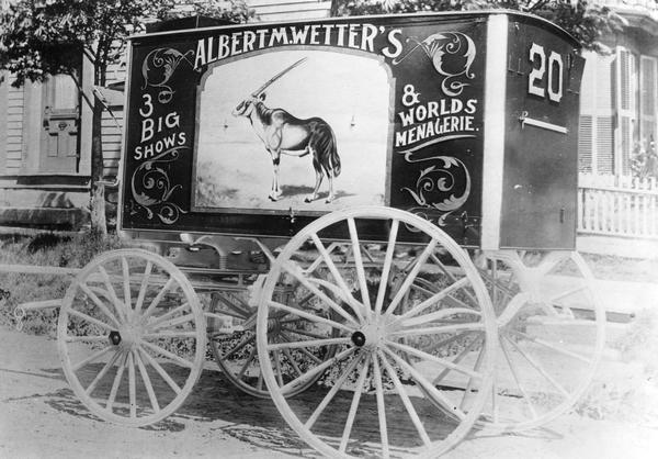 Wagon number 20, advertising Albert M. Wetter's 3 Big Shows & World's Menagerie, is parked at a curb next to a private residence.