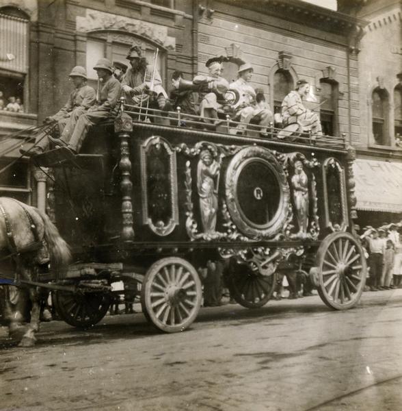 A Ringling Circus wagon, pulled by a horse, with clowns riding on top, is part of a parade along a city street.