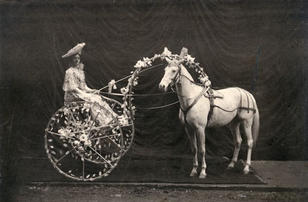 Della Royal (Mrs. Rhoda Royal) sits in a 2-wheeled cart decorated with flowers and harnessed to her world famous horse, "Glendive," as taken from a 1906 handbill.