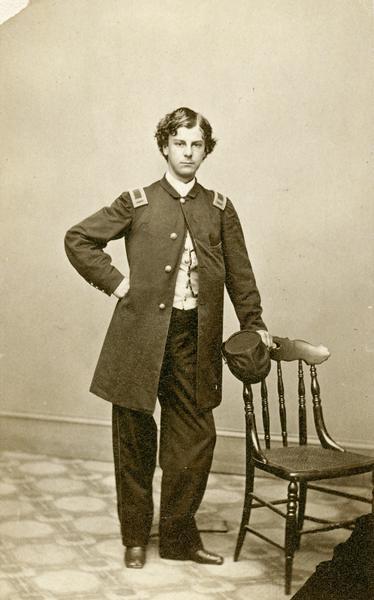 Studio portrait of young Lieutenant Colonel Arthur MacArthur Jr., F & S, 24th Wisconsin Infantry, posing in a Civil War uniform next to a chair.