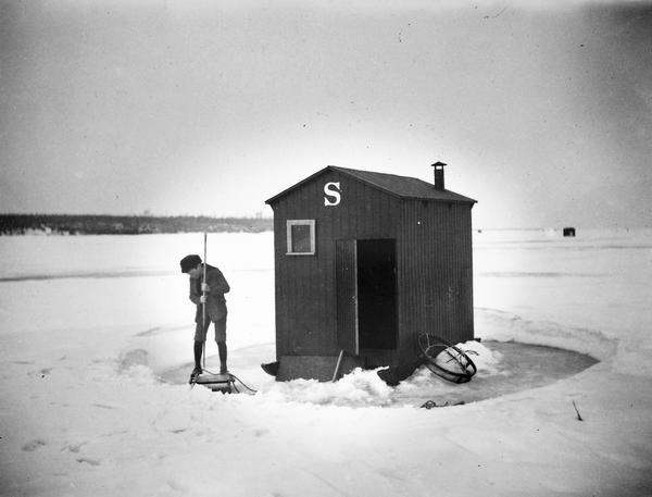A boy dressed in knickers clears the ice in preparation to fish next to his family's ice shanty.