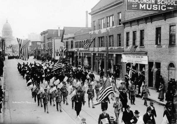 Elevated view of men carrying flags marching down State Street from the Wisconsin State Capitol in a Loyalty Day Parade.