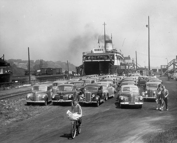 A boy rides his bike as if leading a fleet of cars, with the Lake Michigan ferry blowing smoke in the background.