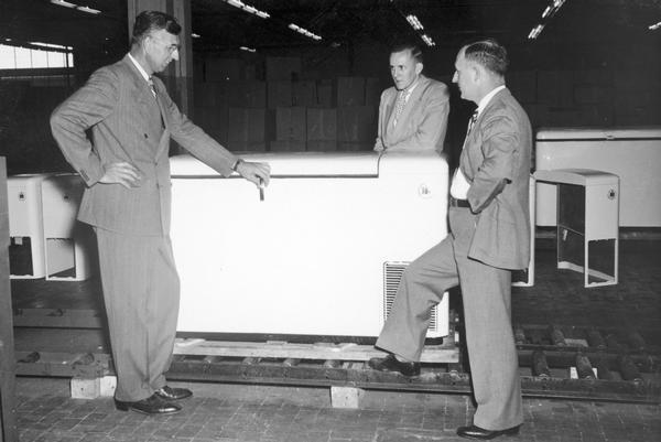 Three executives pose in front of the new International Harvester freezer at International Harvester's Evansville Works. The Evansville Works also produced refrigerators and air conditioners.