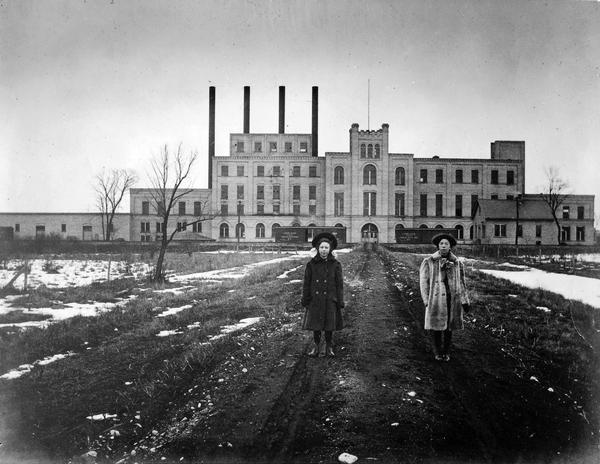 U.S. Sugar Company Two women standing on path in front of the Garver Feed Mill, which was originally a sugar beet processing factory.