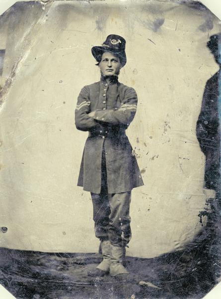 Ferrotype/tintype portrait of Corporal Cornelius Wheeler of Company I of the 2nd Wisconsin Regiment. Standing, facing forward with arms folded, in full uniform. This photograph was probably taken in the field shortly after the regiment received their distinctive Iron Brigade uniforms. On the first day at Gettysburg the Iron Brigade sustained its reputation as a fighting force, despite severe losses. The 2nd Wisconsin experienced a 77% casualty rate, and Wheeler, then a sergeant, ended the day as the most senior man in his company.
