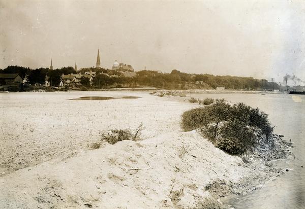View of Madison from Lake Monona with the Wisconsin State Capitol building in the background. This view of Brittingham Park shows a part of the park shortly after if had been filled in by the sand dredge. The photograph was taken from the railroad trestle and looks north-easterly across the triangle-shaped part of the bay.