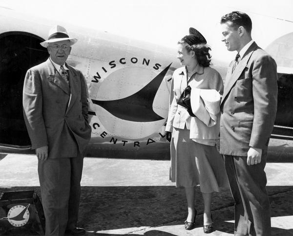 Margaret McGuire, the 1948 Alice in Dairyland, stands next to a Wisconsin Central Airlines airplane with Governor Oscar Rennebohm and another man.