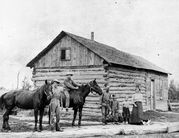 Dutch family posing outside their log home with two horses.