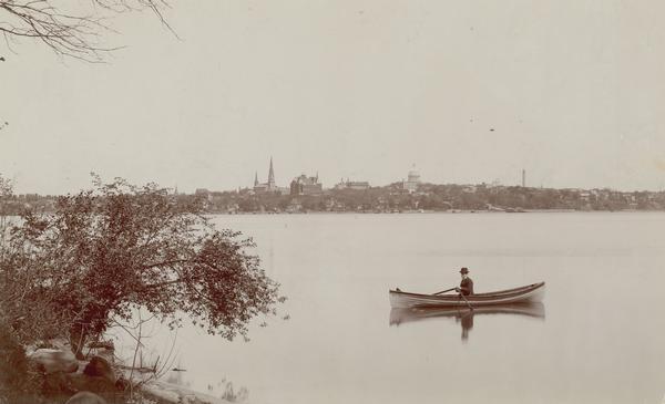 Man in a rowboat on Lake Monona with a view of the city in the background.