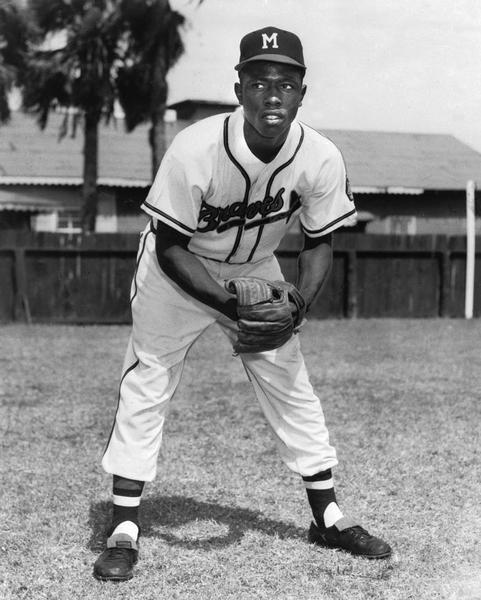 Henry Aaron poses in uniform on a baseball field.