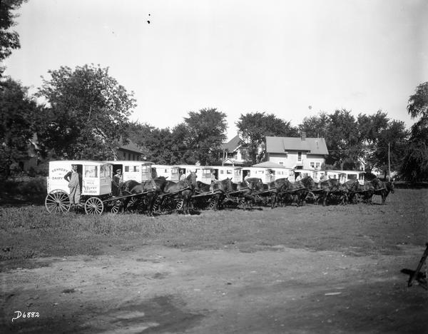 A line of Kennedy Dairy horse-drawn wagons with drivers posing beside them. For Quaker Oats Farm.