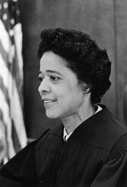 Portrait of Vel Phillips in her judges's black robe with an American flag behind her. She was the 13th District Children's Court judge, the first woman and African American to hold this post.