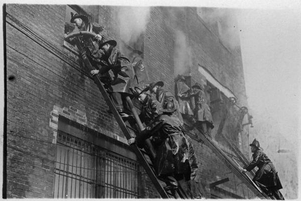 Fire fighters on ladders climbing up to the windows of a burning building.