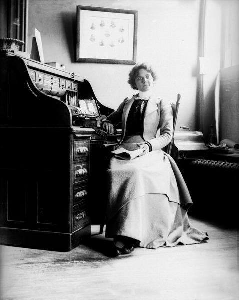 Secretary Jennie Nelson seated at her desk in the offices of the La Follette, Harper, Roe, & Zimmerman law partnership. After Robert M. La Follette, Sr., was elected governor of Wisconsin in 1900, Jennie Nelson went to work for him in the Capitol. It is likely that this photograph was taken by Albert Zimmerman