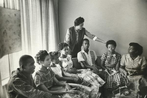 Daisy Bates, the head of the Arkansas NAACP, stands behind seven of the Little Rock Nine, who are seated on a sofa in her living room. They have assembled there to await the arrival of the soldiers of the 101st Airborne Division who will escort them to school. The students are Jefferson Thomas, Carlotta Walls, Thelma Mothershed, Gloria Ray, Terrence Roberts, Elizabeth Eckford, and Melba Pattillo.