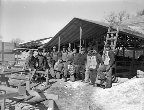 A group of workmen posing in front of the First Unitarian Society Meeting House during construction. This is one of two "work days" the men donated to the construction of the building. The building was designed by Frank Lloyd Wright and built by Marshall Erdman with some assistance from members of the congregation.