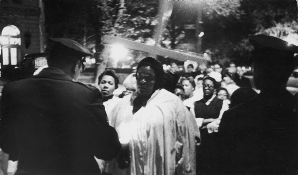 Members of the National Welfare Rights Organization, some dressed in choir robes, hold candles and a cross as they are confronted by police. This is at the entrance to the United States Capitol where the group held a vigil in memory of Dr. Martin Luther King, Jr. after his assasination. Thirty-five of the NWRO leaders and three ministers were arrested for "assembling to sing and pray".