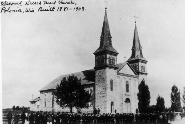 Exterior view of the second Sacred Heart Church, which was built in 1881-1903. A large crowd, probably parishioners, pose in front of the building.