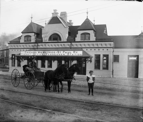 Chicago Milwaukee and St. Paul Depot Exterior view of the Chicago, Milwaukee and St. Paul Railroad depot on the corner of Wilson and Franklin Streets, designed by Edward Townsend Mix. There are people and a horse-drawn carriage in front of the depot.