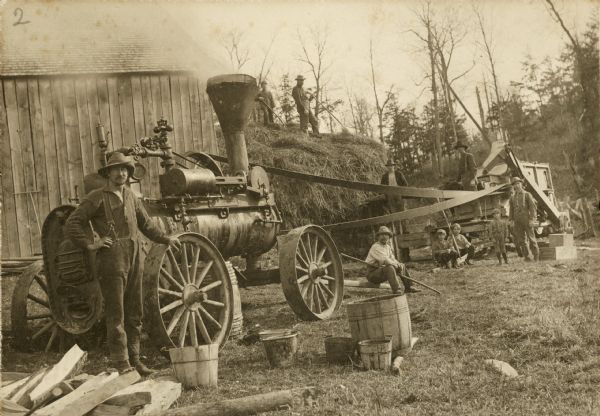 Men and boys posing around a threshing steam tractor. Oliver Johnson is in the foreground. John Bergeson and Art(?) are on top of the stack. Henning Bergeson standing near the thresher.