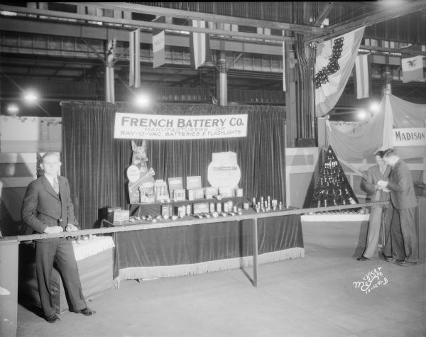 French Battery Co. booth at East Side Business Men's Association (ESBMA) Fall Festival. "Manufacturers of Ray-O-Vac batteries and flashlights."  Featuring two men looking at flashlights, and another man standing on the left.