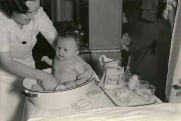 Dr. Hunter of the Wisconsin Board of Health bathes a baby in a tub of water.