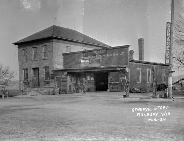 Exterior view of the general store and automotive garage in Roxbury. A man and woman, possibly the owners, are standing in front of the buildings.