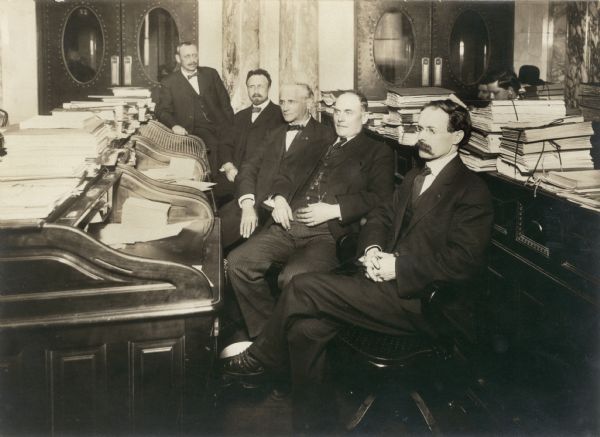 Newly elected assemblymen in the newly constructed Assembly Chamber of the present Wisconsin State Capitol.  On the right is Merlin Hull of Black River Falls, later secretary of state and U.S. congressman.  Others with him include Walter Egan of Superior, C.E. McConnell of La Crosse, and Frank Hannumill of Spooner.  The legislators are sitting at desks from the Third Capitol, suggesting that a substantial number were rescued from the flames during the fire of 1904.  The old desks were sold in 1913 when new furniture was purchased.