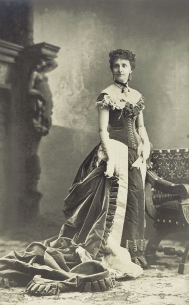 Portrait in front of a painted backdrop of Frances (Bull) Fairchild (1845-1924), wife of Wisconsin Governor Lucius Fairchild, wearing a court gown designed by Charles Frederick Worth of Paris, France. Worn at the Spanish court of King Alfonso XII and Queen Teresa, Madrid, Spain, 1880.
