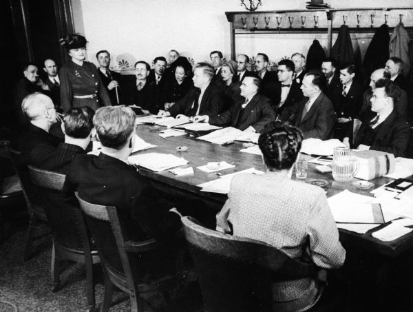 A woman stands before an assembly committee meeting in an executive session.